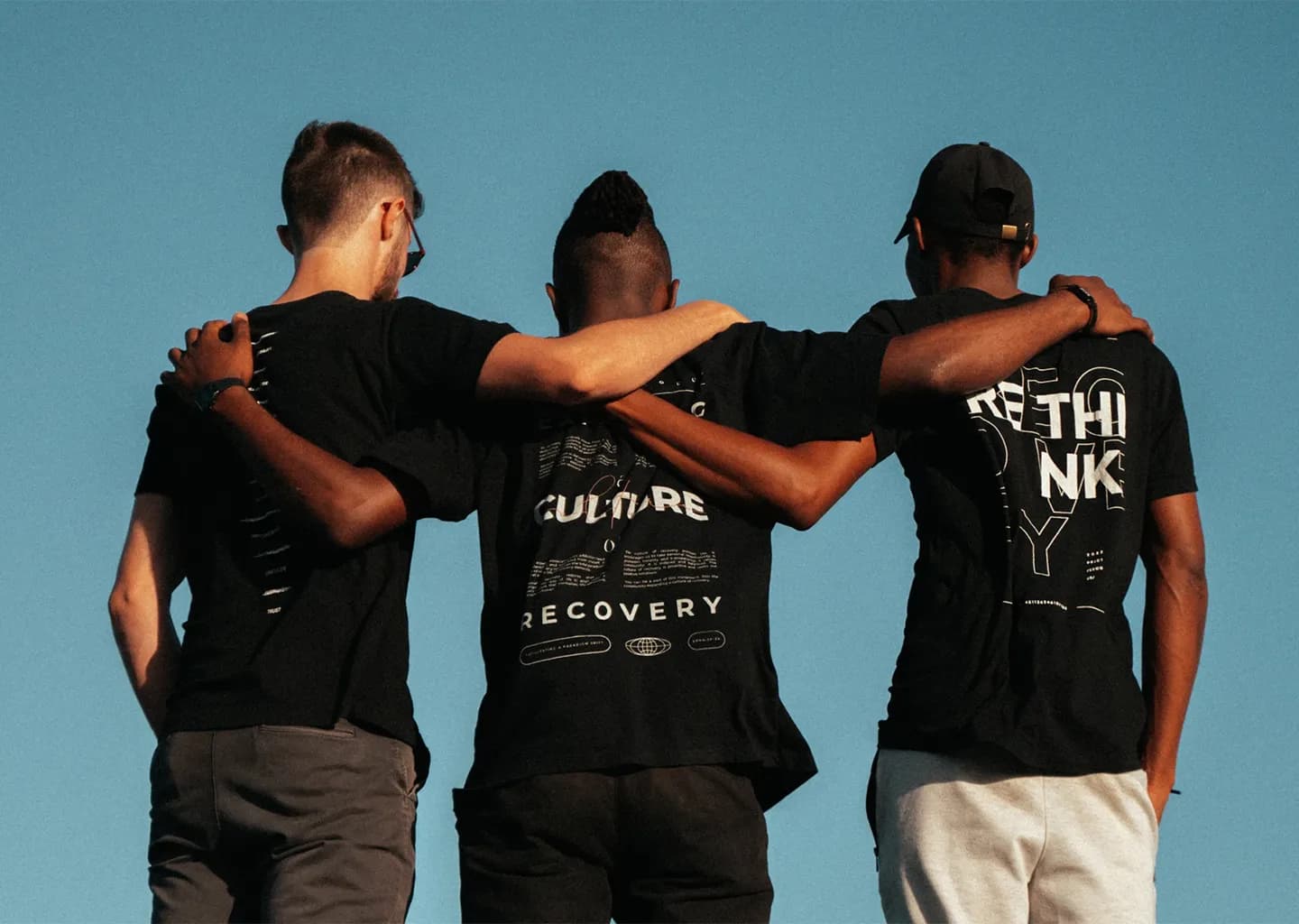 Three men in black shirts standing together with arms around each other.