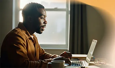 A man sits at a desk, focused on his laptop.