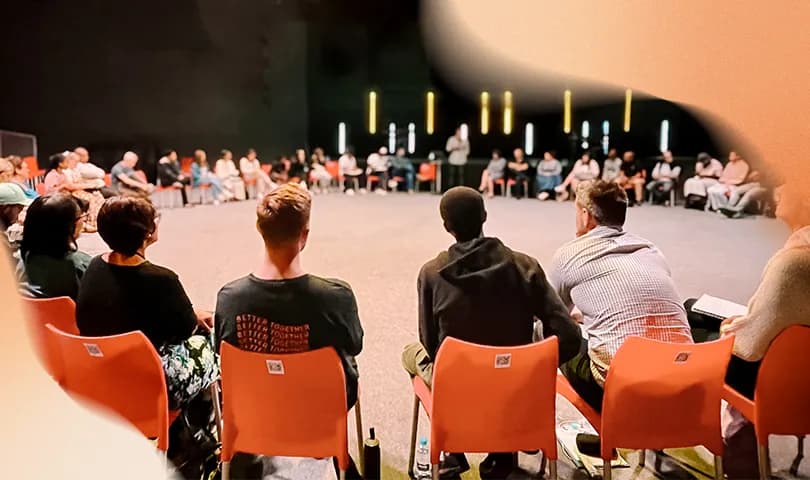 A group of people sitting in a circle in chairs participating in a recovery group.