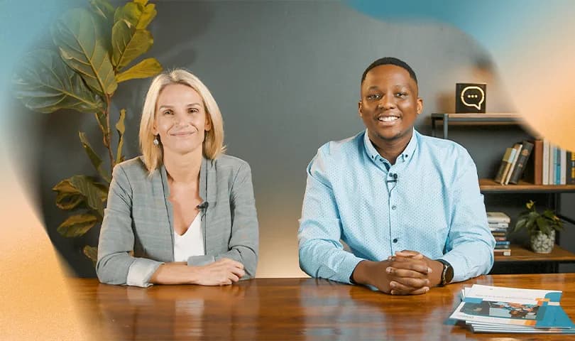 A man and woman sitting behind a desk looking forward and smiling.
